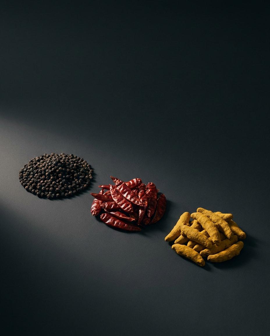 Separate heaps of black peppercorns, dried red chillies and turmeric fingers